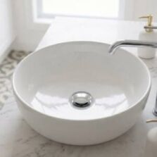 A modern chrome pop-up waste installed in a white ceramic bathroom basin next to a matching basin mixer tap