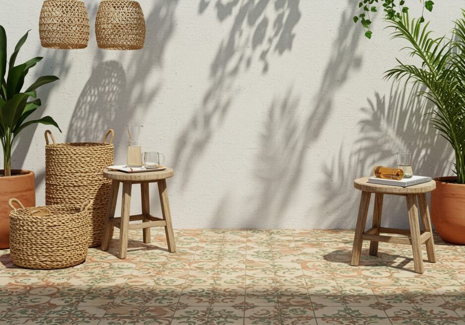 A Mediterranean-inspired outdoor space showcasing patterned tile trends with intricate floral designs in warm terracotta and green tones, complemented by wooden stools, woven baskets, and lush greenery.