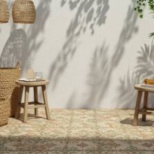 A Mediterranean-inspired outdoor space showcasing patterned tile trends with intricate floral designs in warm terracotta and green tones, complemented by wooden stools, woven baskets, and lush greenery.