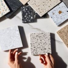 hands holding terrazzo tile samples with natural and porcelain look terrazzo tiles on marble surface