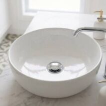 A modern chrome pop-up waste installed in a white ceramic bathroom basin next to a matching basin mixer tap