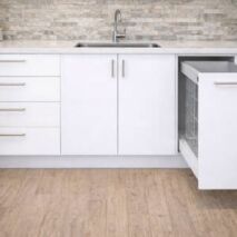 White kitchen base cabinets with integrated drawers, sink unit, and pull-out wire basket, set beneath a stone benchtop and tiled splashback.