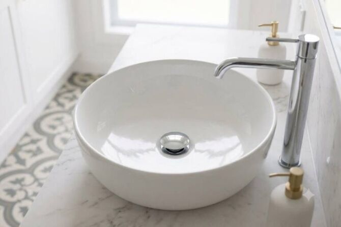 A modern chrome pop-up waste installed in a white ceramic bathroom basin next to a matching basin mixer tap